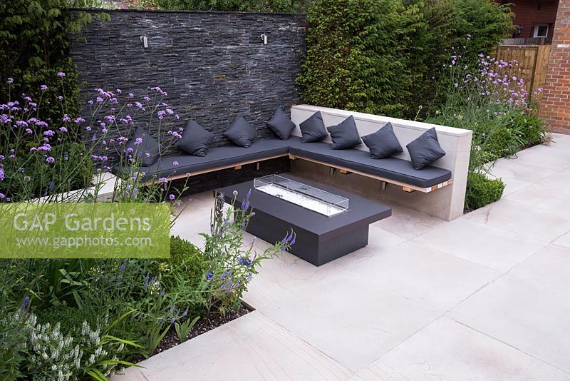Secluded seating area with a dry stone slate wall and propane fire pit. Featuring sunken planting of Verbena bonariensis, Veronica and Agapanthus