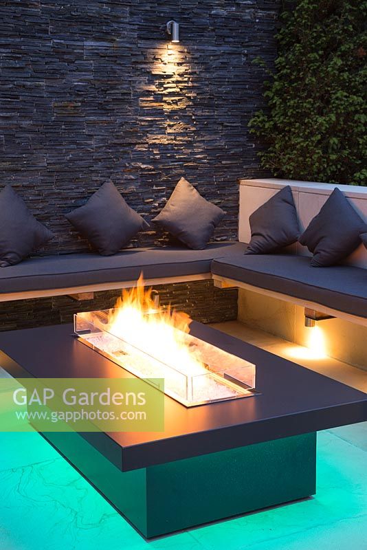 Secluded seating area with a dry stone slate wall and propane fire pit emitting cyan light