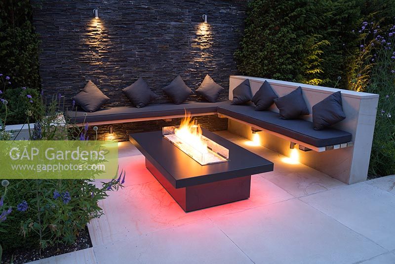 Secluded seating area with a dry stone slate wall and propane fire pit emitting red light