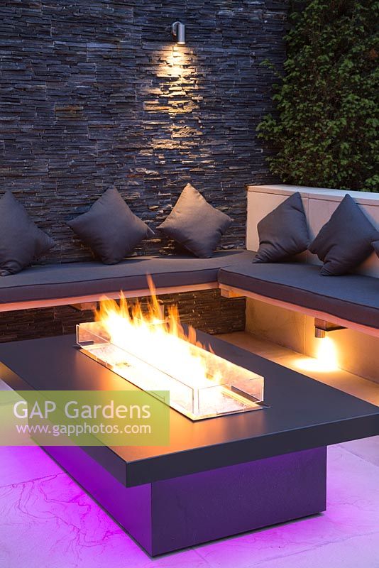 Secluded seating area with a dry stone slate wall and propane fire pit emitting purple light