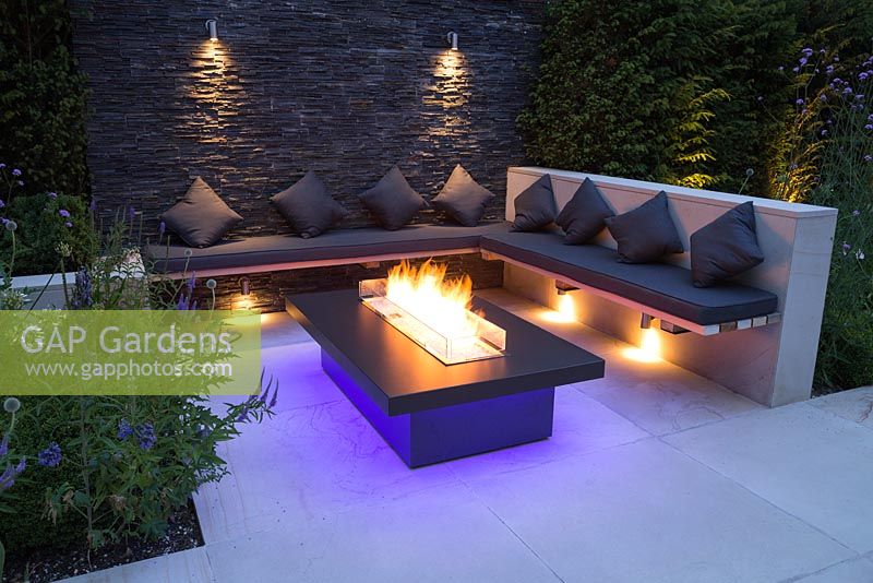 Secluded seating area with a dry stone slate wall and propane fire pit emitting blue light