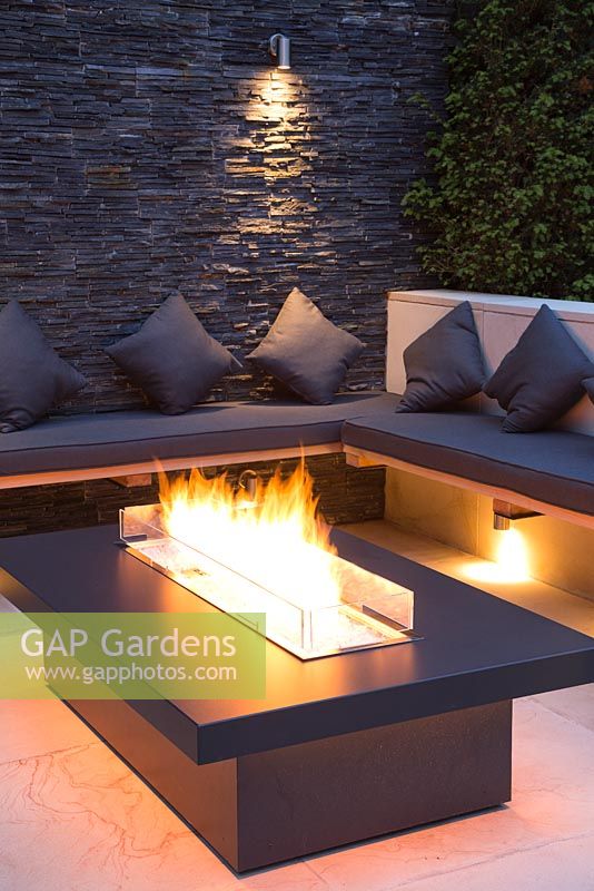 Secluded seating area with a dry stone slate wall and propane fire pit emitting orange light