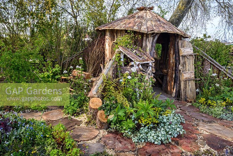 Wooden hut and log store with Ajuga, Lamium, Euphorbia and Heuchera - The Woodcutter's Garden, RHS Malvern Spring Festival 2016. Design: Mark Walker