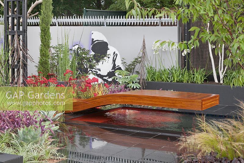Contemporary wooden half bridge over water feature set into glossy, black tiles. Save a Life, Drop the Knife - RHS Tatton Flower Show 2011, Cheshire