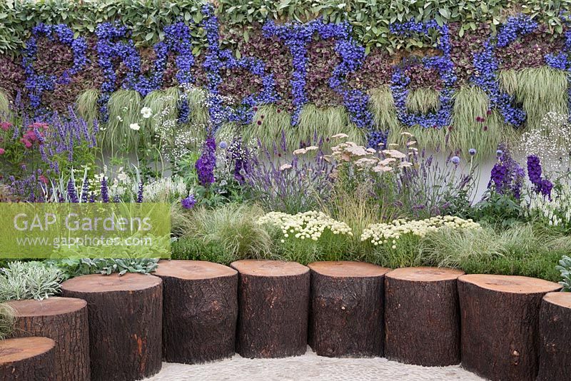 A living wall with blue, purple and white planting and rustic log seating. Embrace, RHS Tatton Flower Show 2011, Cheshire