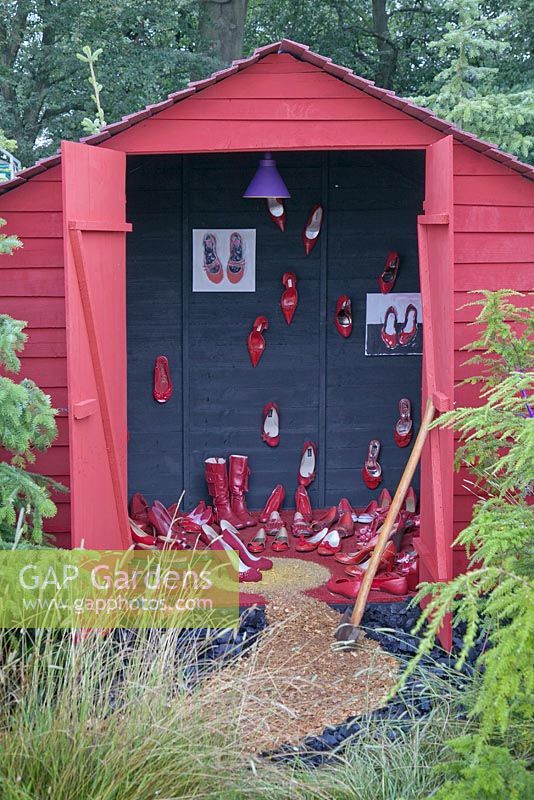 A red painted shed full of red shoes in a woodland setting. Fairy Tale, RHS Tatton Flower Show 2011, Cheshire