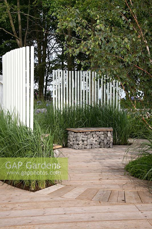 Grasses, white wooden slatted fence and gabion seat. Garden: 'A Prison Garden For Rehabilitation' at RHS Tatton Park Flower Show 2012