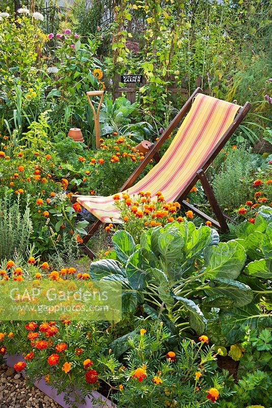 Deckchair in kitchen garden. Raised beds full of vegetables, herbs and flowers.