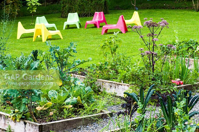 Plastic chairs on the lawn with raised beds in the foreground for growing salads. Hunting Brook Garden, Co Wicklow, Ireland