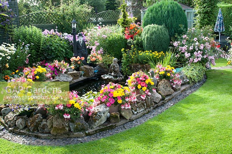 Colourful back garden with pond and rockery mixed borders filled with tender bedding plants, shrubs and perennials. 