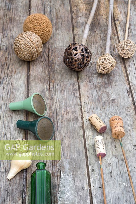 A variety of materials that can be used as cane toppers. Woven balls, tennis balls, wine corks, seashells, glass vases and bottles