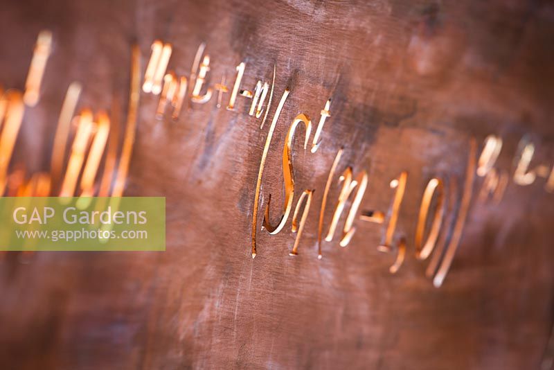 Mathematical symbols cut into a band of copper running through the Winton Beauty of Mathematics Garden, RHS Chelsea Flower Show 2016. Used as backing to seat and staircase bannister