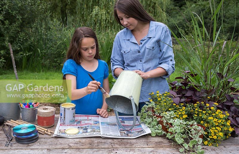 Two girls painting a galvanised bucket with a cream green paint