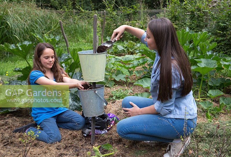 Two girls filling galvanised buckets with compost