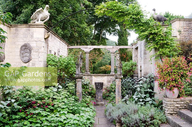 West end of the Great Terrace with views through to surrounding countryside, pair of Italian dancing figures and arch with Wisteria, plants include Lavandula, Geranium, Fuchsia and Begonia fuchsioides in pots