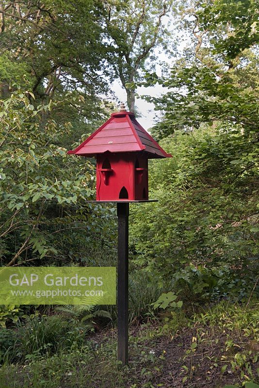 Red painted wooden bird house in woodland - June, Clyne Gardens, Swansea, Wales