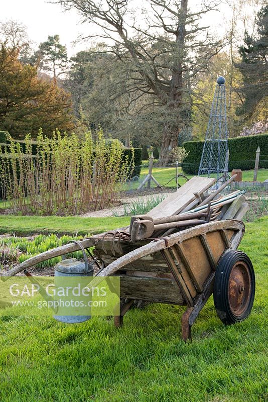 Old wooden wheelbarrow in the kitchen garden with metal watering can