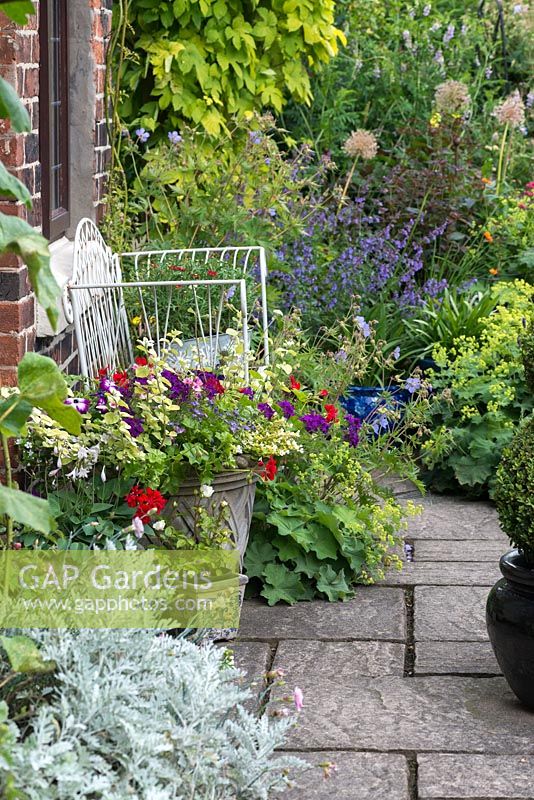 A cottage garden with stone path leading to a metal bench and containers planted with annuals