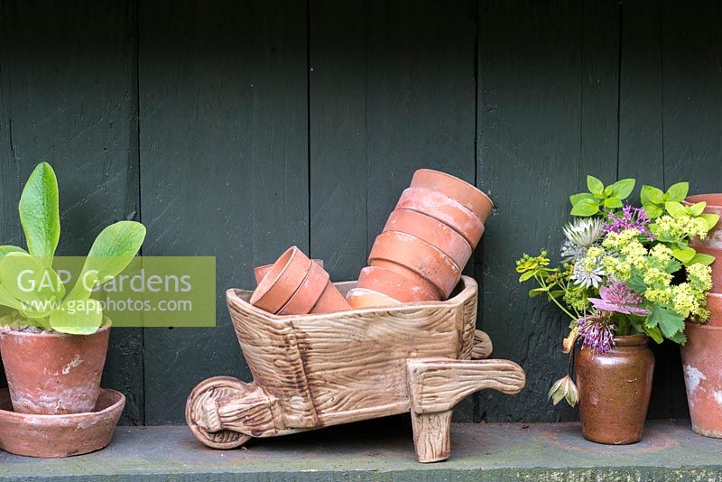 A shelf with model wheelbarrow, terracotta pots and a posy picked from the garden.