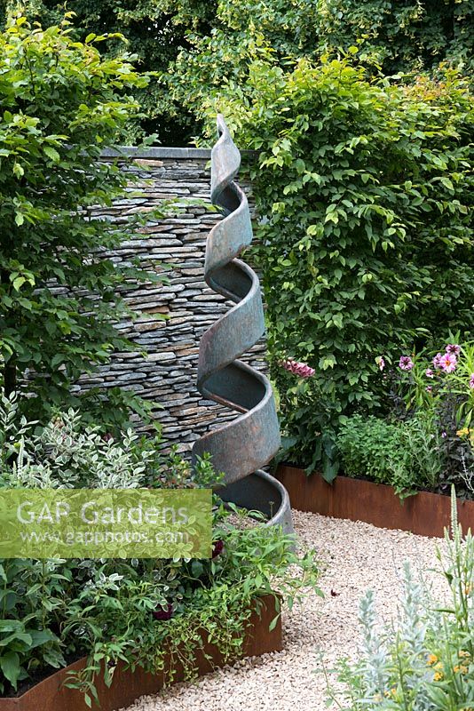 An Arts and Crafts inspired garden with spiral sculpture by Giles Rayner, hornbeam hedge and raised corten steel borders. A Summer Retreat designed by Laura Arison and Amanda Waring. Hampton court flower show 2016