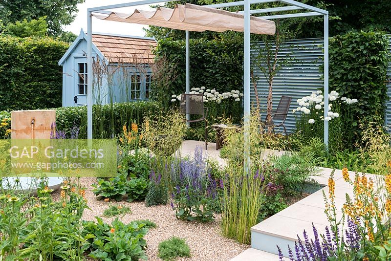 A enclosed contemporary town garden with stone patio, steel pergola with retractable shade, painted shed and a gravel bed planted with perennials and grasses. A Retreat Garden designed by Martin Royer.