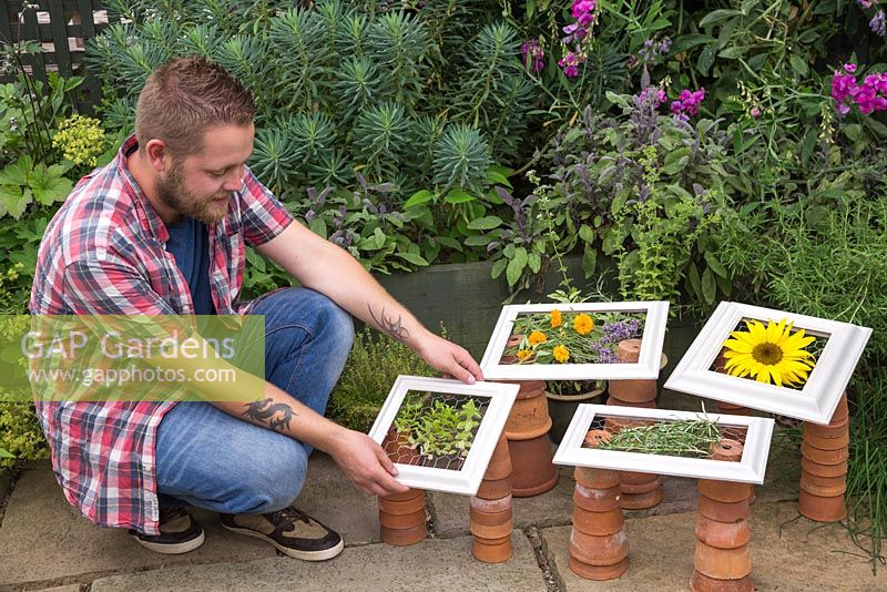 Man placing drying frames with herbs and flowers on top of terracotta pots