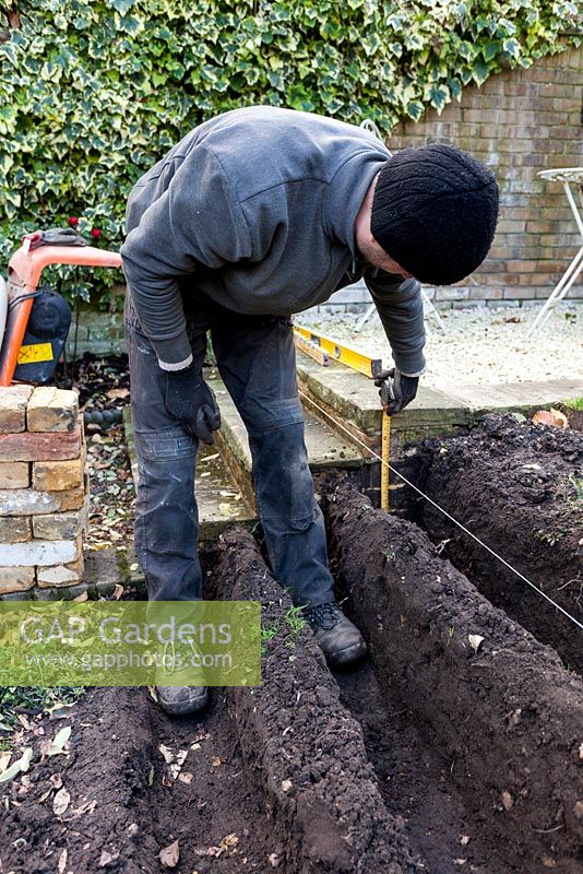Construction of stepped border in London garden - the first foundation trenches being dug, with the builder measuring depth