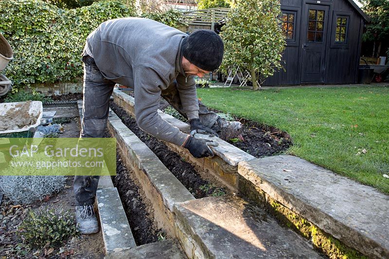 Stepped border in London garden -  landscaper fixing York stone to wall with cement