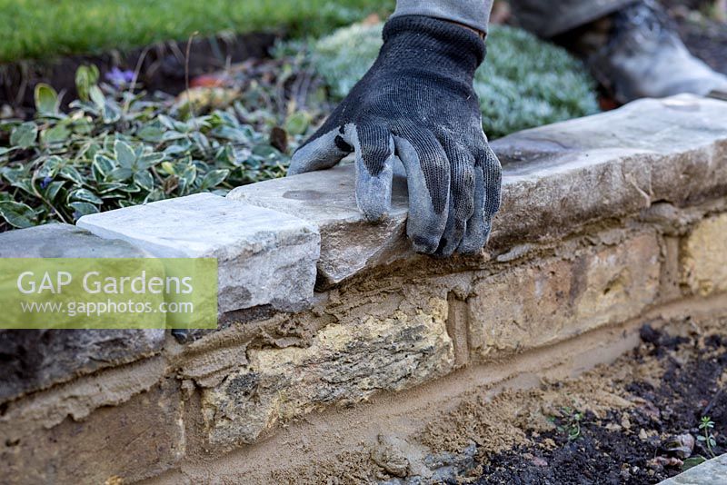 Stepped border in London garden -  landscaper checking York stone is square on the wall using spirit level