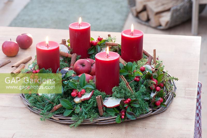 Advent wreath from Chamaecyparis and Gaultheria procumbens, decorated with red candles, dried apple slices, cinnamon sticks and apples 
