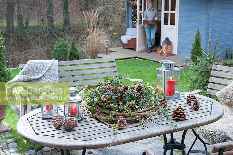 Garden table decorated with wreath of Clematis vines with Gaultheria procumbens, Hedera and cones, lanterns and pine cones

