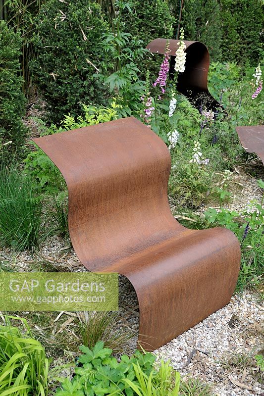 Contemporary curved metal seat in a cottage garden'Nous irons tous au jardin' designed by Laurent Dabomprez and Gaelle Van Damme at the Festival International des Jardins 2016, Chaumont-sur-Loire, France