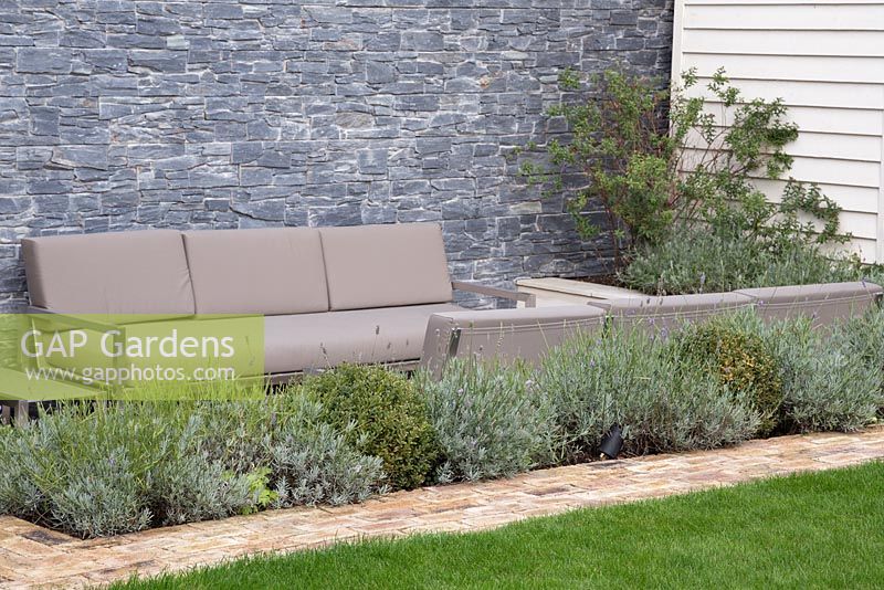 Sunken seating area backed by a dry stone slate wall and a border of Lavandula angustifolia 'Munstead' and Buxus sempervirens