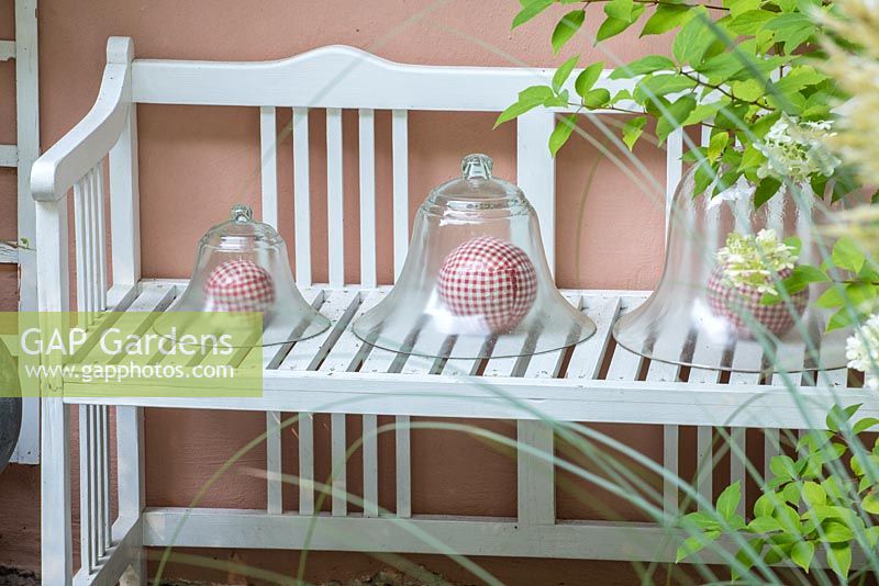 Decorative bell jars with red and white chequered spheres on a white wood bench