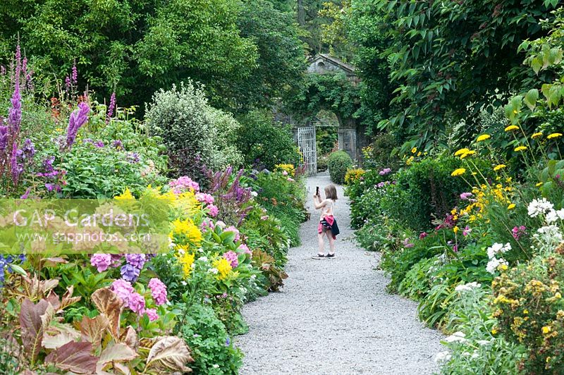 The Walled garden with herbaceous borders and young girl taking a picture in the Gardens of Ilnacullin - Garinish Island. Glengarriff, West Cork, Ireland. The Gardens are the result of the creative partnership of Annan Bryce and Harold Peto, architect and garden designer. August
