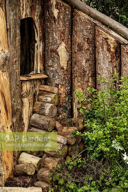 Edge of rustic wooden hut with stacked log pile - The Woodcutter's Garden - RHS Malvern Spring Show 2016. Designer: Mark Walker, Sponsor: Howards Motors