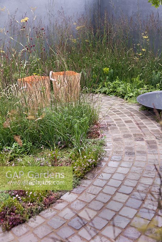 A naturalistic planting of grasses and perennials enclose a stone cobbled seating area with shallow water bowl - July, 'A Quiet Corner' at RHS Tatton Flower Show 2015