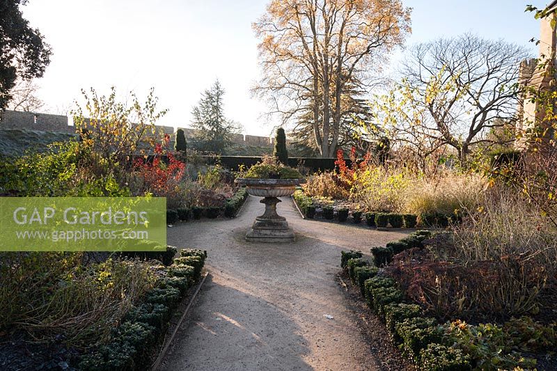 The formal East Garden at the Bishop's Palace garden in Wells, with decorative urn and beds edged with evergreen euonymus planted with a mix of herbaceous perennials and shrubs including red leaved cotinus