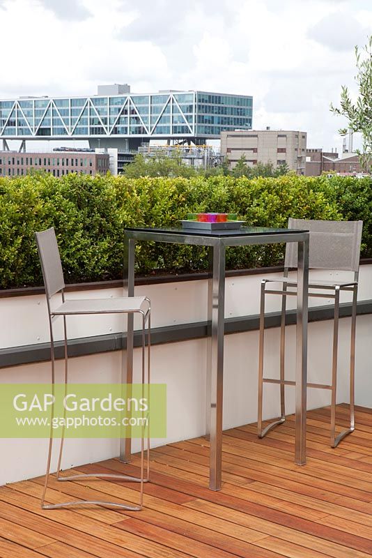 Roof garden with decking terrace, bar stools and table. View on the city Rotterdam, Holland.