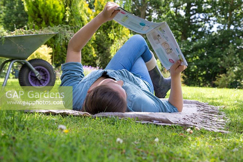 Young girl laying on a rug reading a magazine in the garden