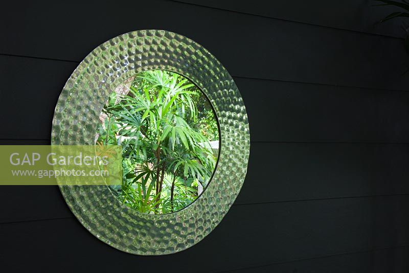 Patterned mirror on wall reflecting green garden foliage