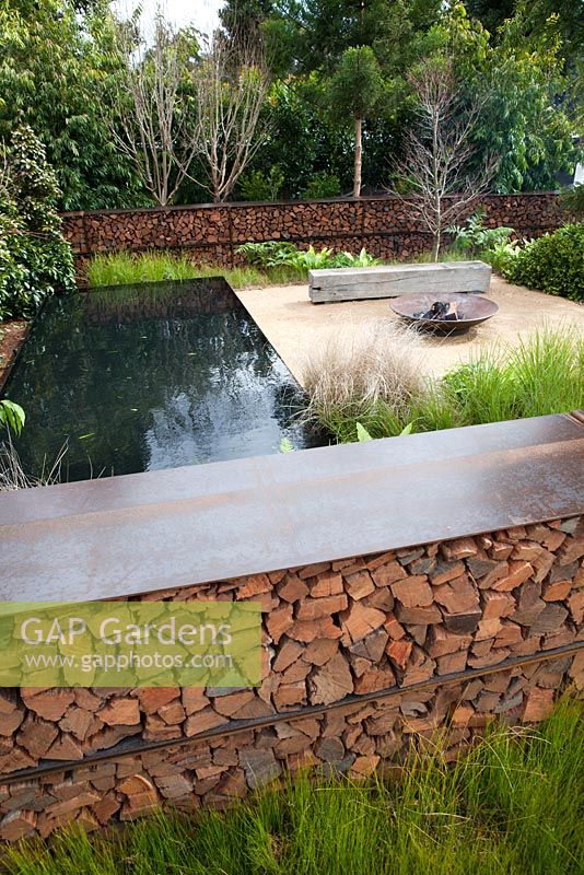 A garden with a fire pit, timber seating area  and pond