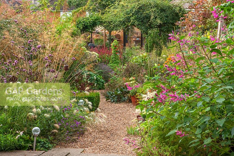 Gravel path, rusty metal allium sculptures, pennisetum villosum, verbena bonariensis, stipa gigantea.  Owner of Daisy Roots Nursery, Anne Godfrey's private garden, Hertfordshire. 