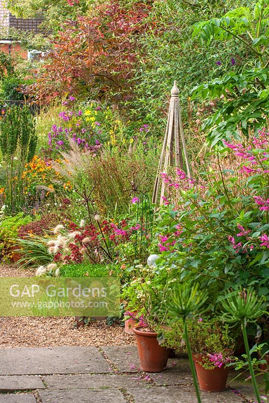 Gravel path, metal chicken ornament, sedum pennisetum, wooden support, salvia bethellii.  Owner of Daisy Roots Nursery, Anne Godfrey's private garden, Hertfordshire. 