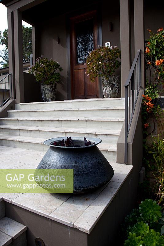 A black glossy cauldron style pot on a landing at the front entrance of a house