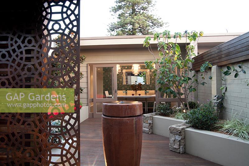 Inner city courtyard with a freestanding ceramic water feature, a rusty decorative screen, a raised garden bed,a raised garden bed with a combination of cement rendered and stacked stone wall, featuring a Cercis tree.