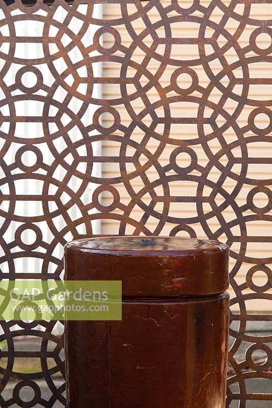 Ceramic water feature in a small courtyard garden in front of a steel decorative screen