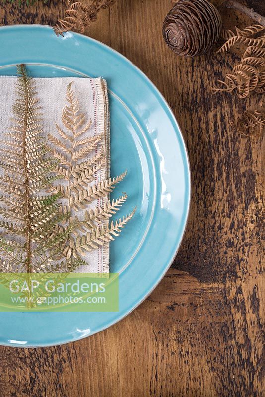 A table place setting with gold spray painted Fern fronds on a teal plate