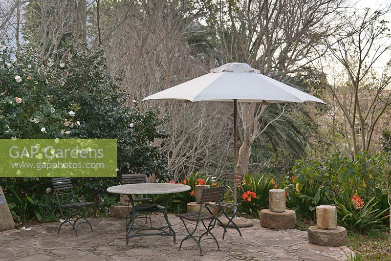 Outdoor wood and metal table and chairs with white parasol on patio area with Camellia and Clivia miniata - September, The Vineyard Hotel, Cape Town, South Africa 