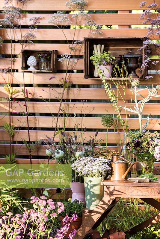 Wooden fence with shelves, work table with bouquets in pots and containers surrounded by summer flowers including Astrantia 'Pink Pride' and Valeriana officinalis. Katie's Lymphoedema Fund: Katie's Garden, Designers: Carolyn Dunster, Noemi Mercurelli, RHS Hampton Court Palace Flower Show 2016 